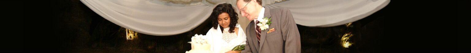 Bride and groom share a moment together, gazing at their wedding cake under soft lighting, emphasizing their celebration of love and commitment.